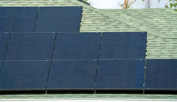 Close aerial view of dark solar panels installed flush on a green shingle roof